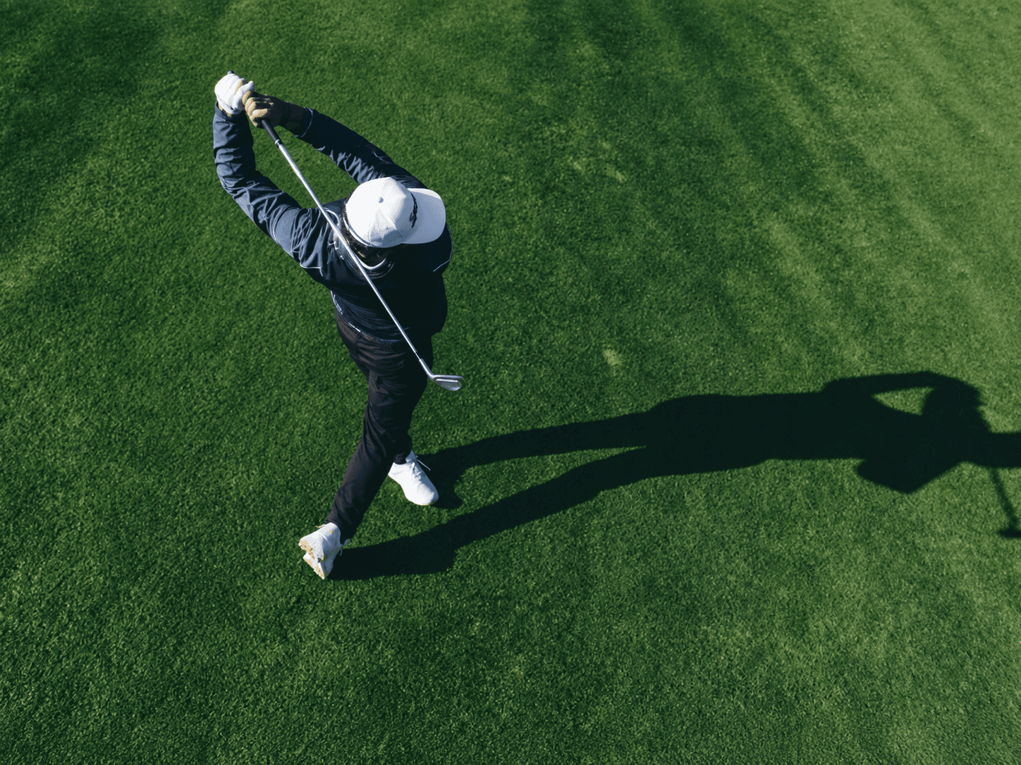 Golfer beim Abschlag auf grünem Rasen, von oben fotografiert